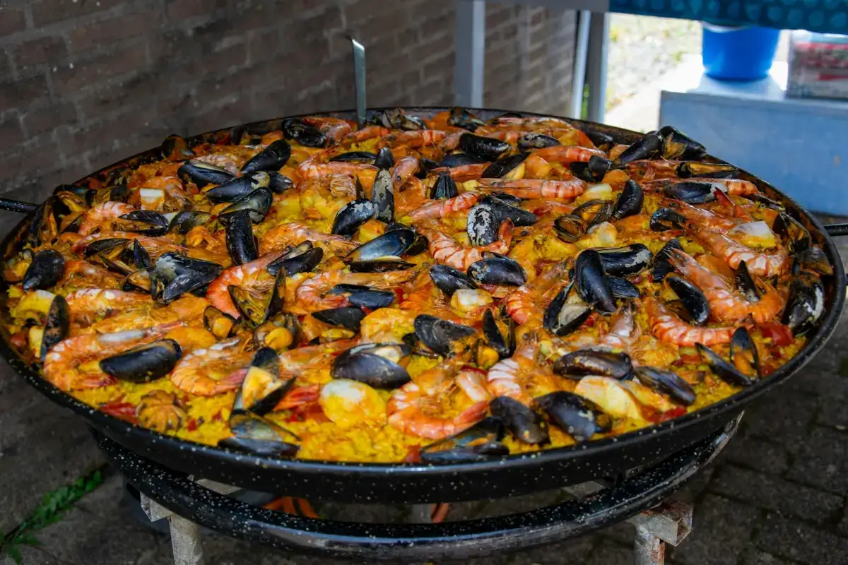 A giant pan of seafood paella cooking over a burner